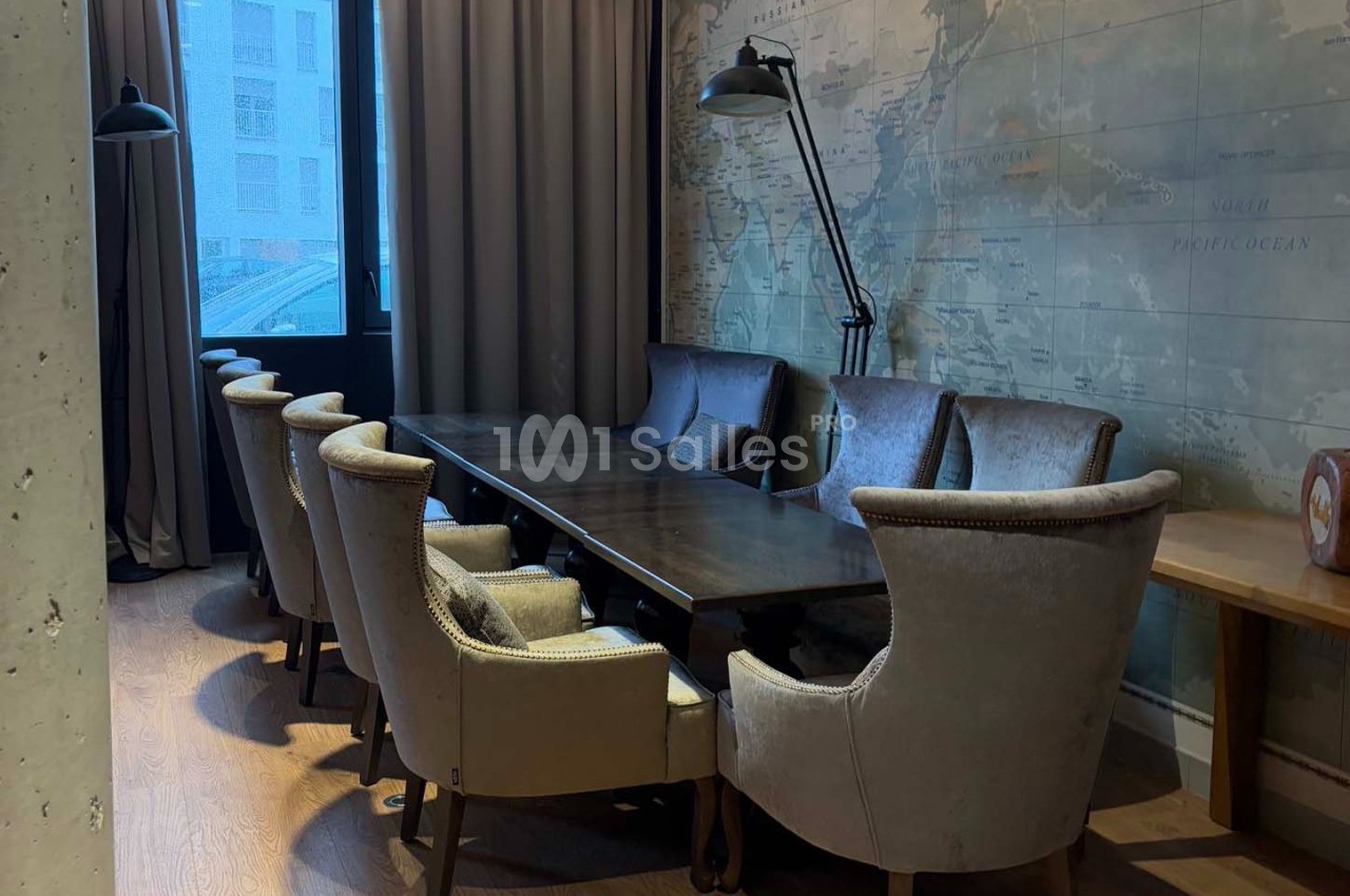 Salle de réunion avec une grande table en bois, entourée de fauteuils rembourrés, éclairée par une lampe et une fenêtre.