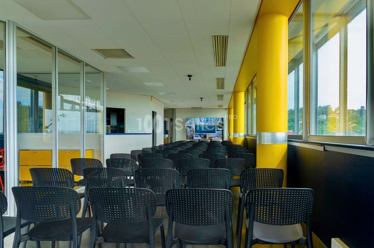 Salle de conférence lumineuse avec rangées de chaises noires alignées face à un écran au fond de la pièce.
