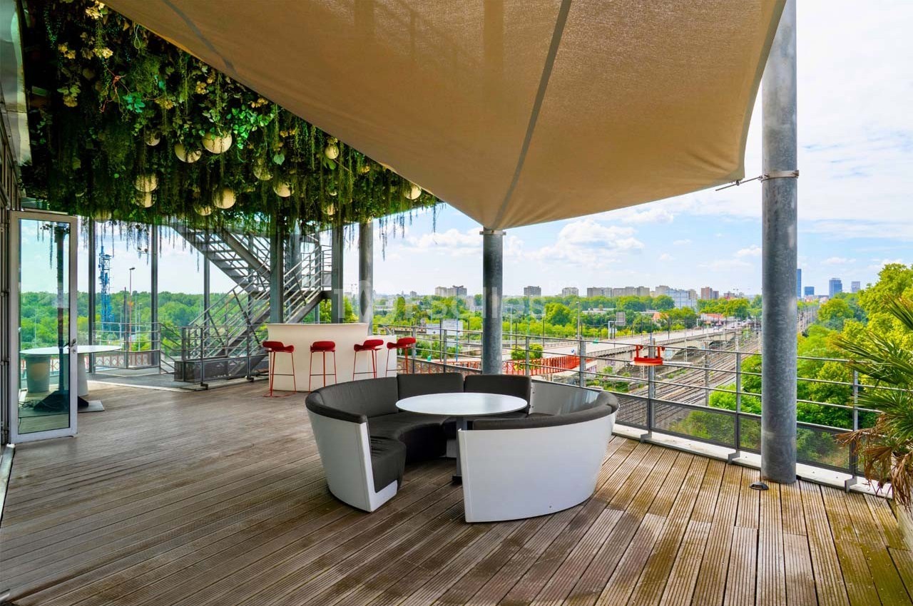 Terrasse en bois avec mobilier moderne, vue sur la ville, végétation suspendue et voile d'ombrage.