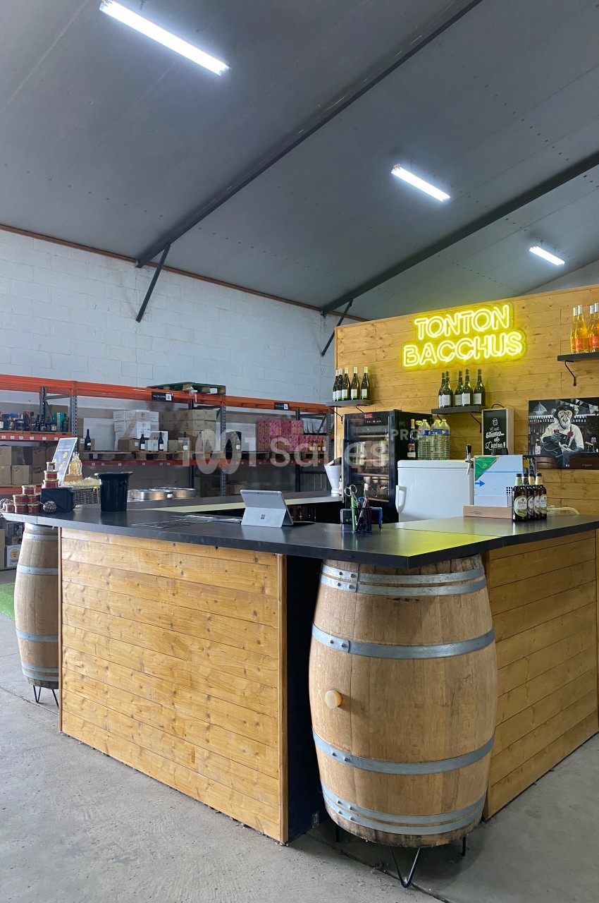 Comptoir en bois avec tonneaux, situé dans un espace de vente, éclairé par un néon ’Tonton Bacchus’.