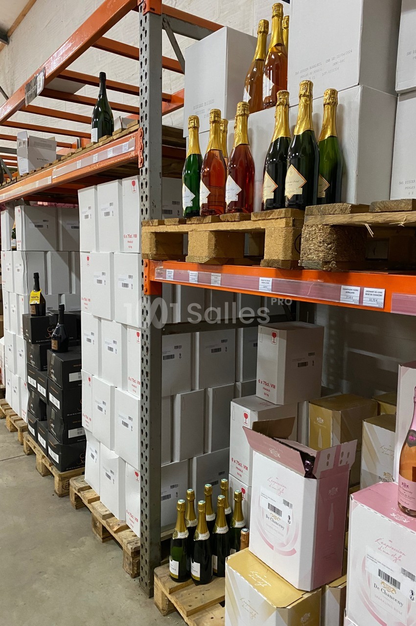 Rayonnages d'entrepôt avec des cartons de bouteilles de vin et de champagne empilés sur des palettes.