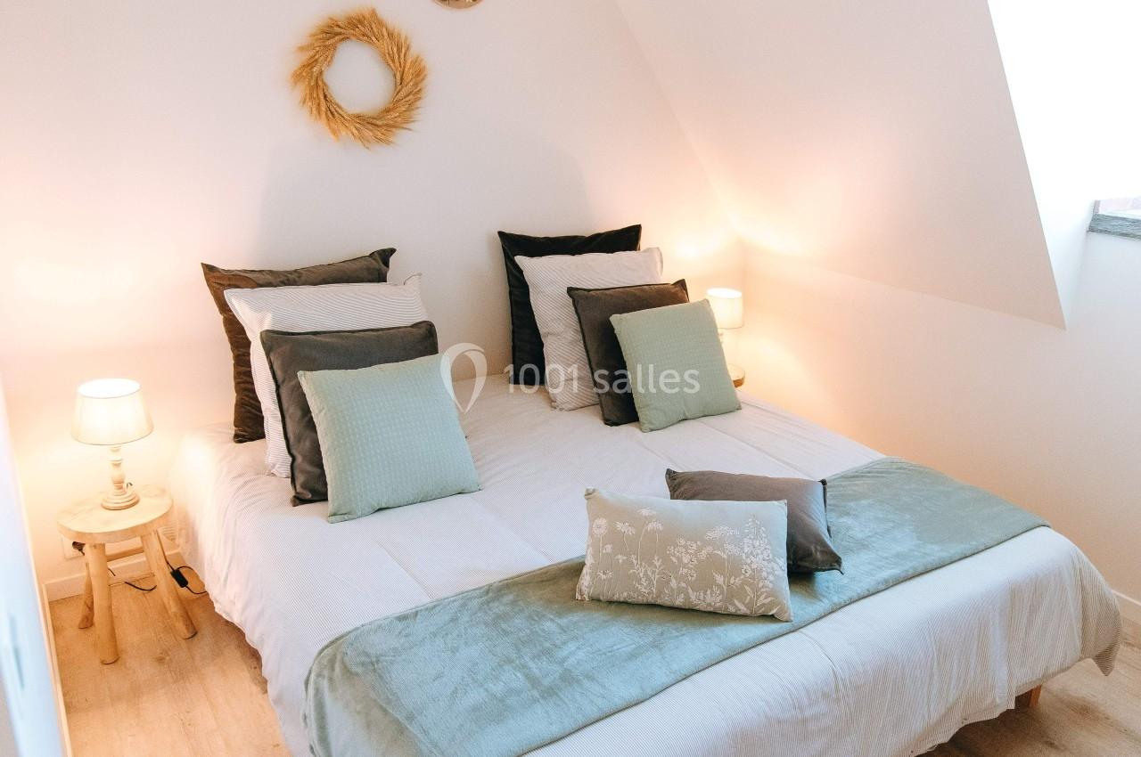 Lit double avec coussins et plaid dans une chambre lumineuse, décorée avec une couronne murale et des lampes de chevet.