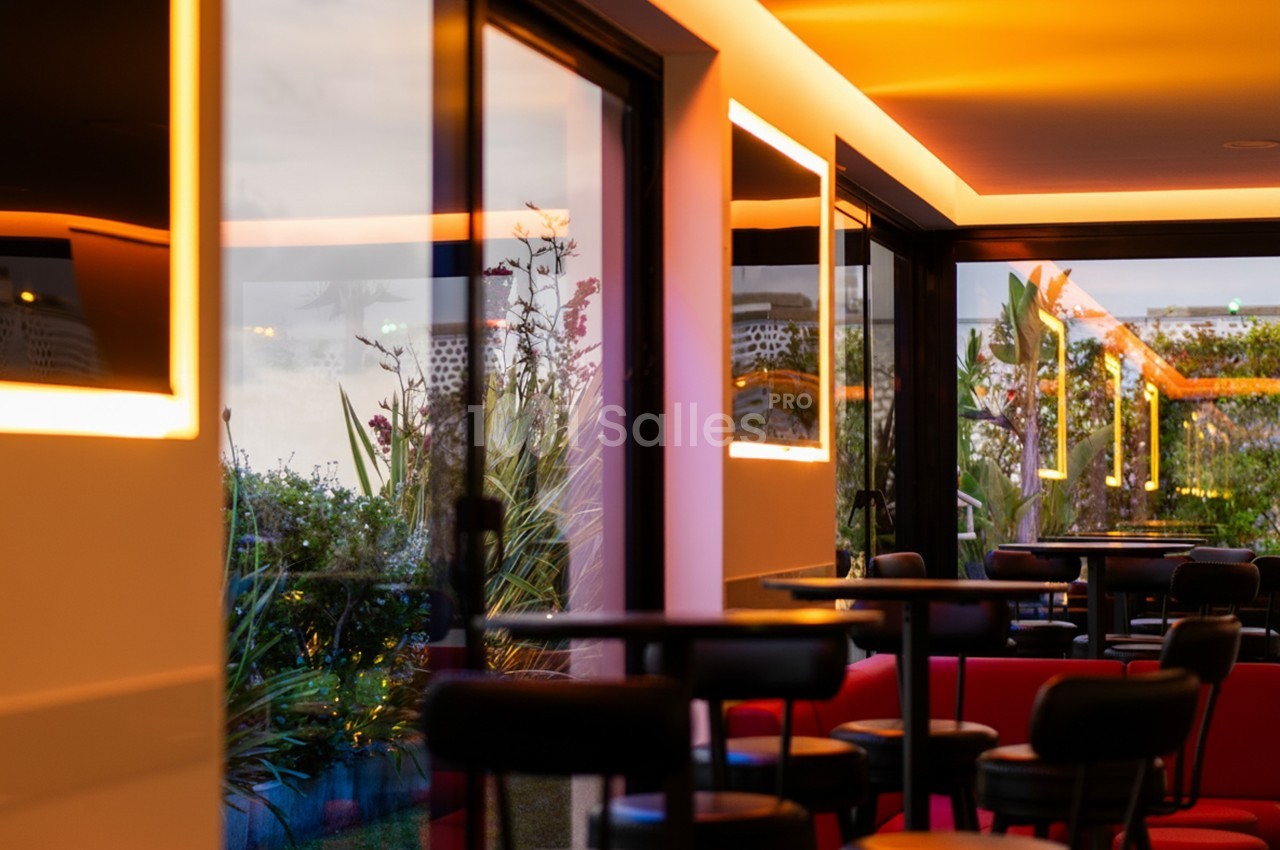 Salle moderne avec grandes baies vitrées, éclairage chaleureux et vue sur un jardin extérieur.