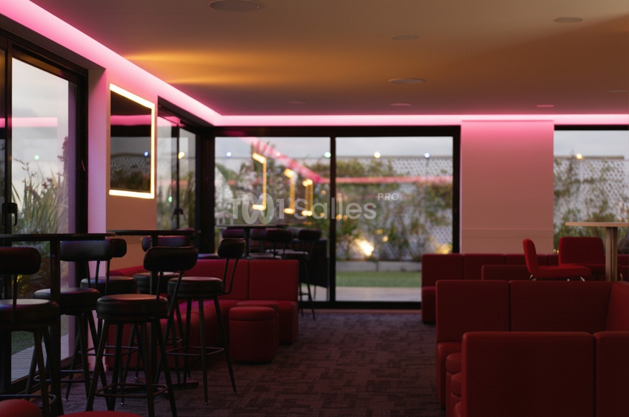 Salle moderne avec éclairage LED rose, mobilier rouge et noir, grandes baies vitrées donnant sur un espace extérieur.