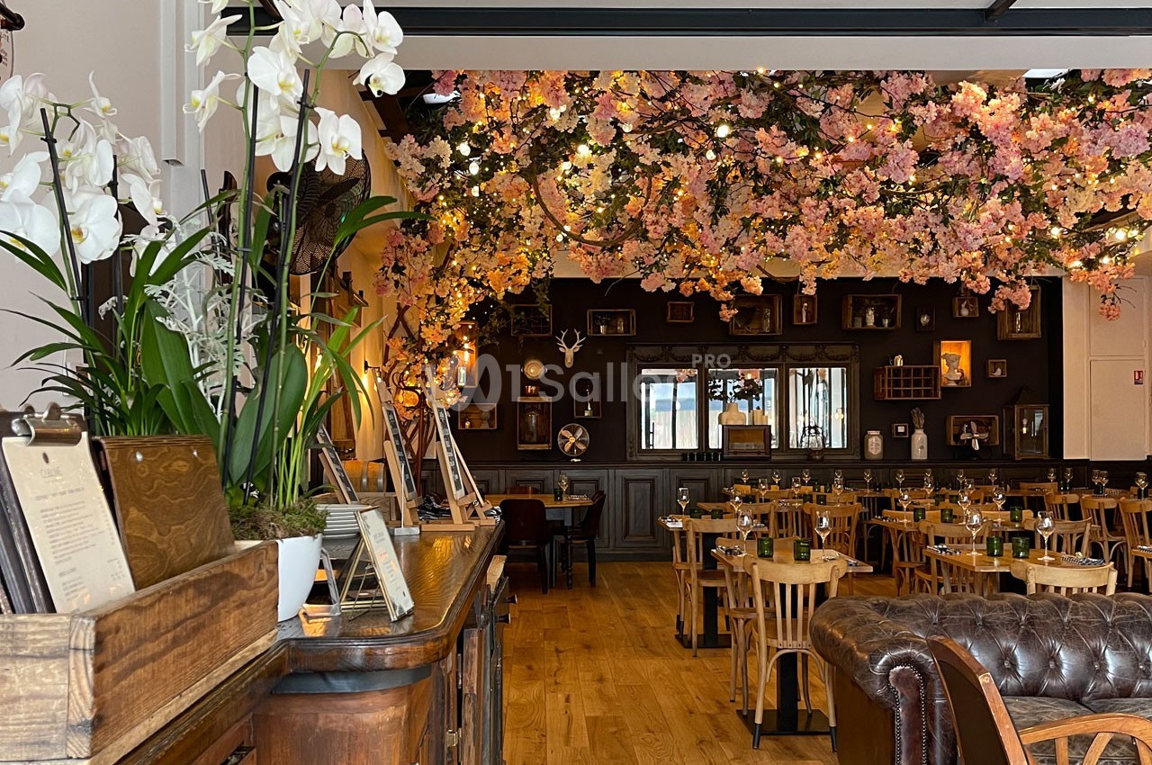 Salle de restaurant décorée avec des fleurs suspendues, des tables en bois et un comptoir avec des orchidées blanches.