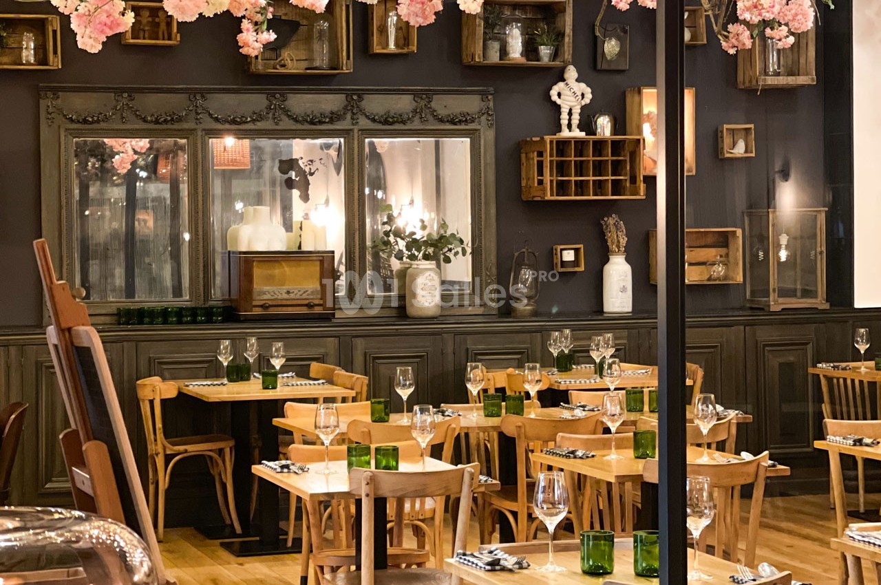 Salle de restaurant chaleureuse avec tables en bois, décoration vintage et fleurs suspendues.