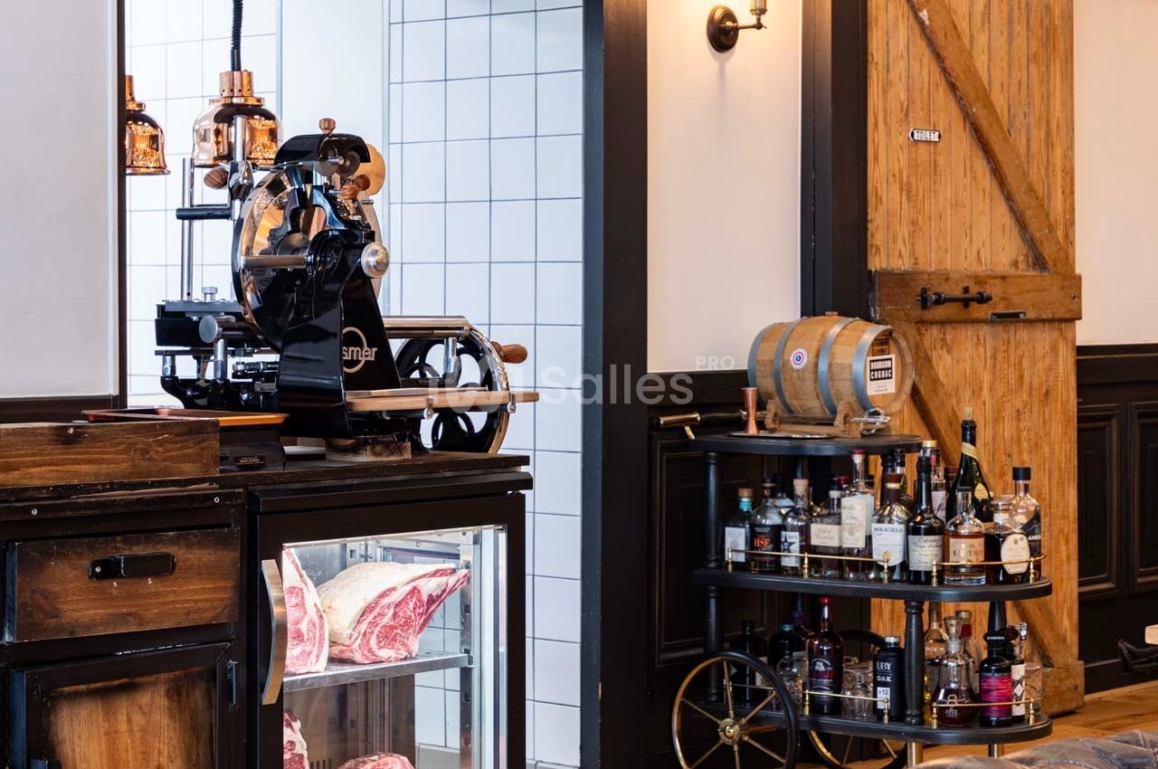 Trancheuse vintage, vitrine réfrigérée avec viandes, chariot de boissons et décor rustique en bois et carrelage blanc.