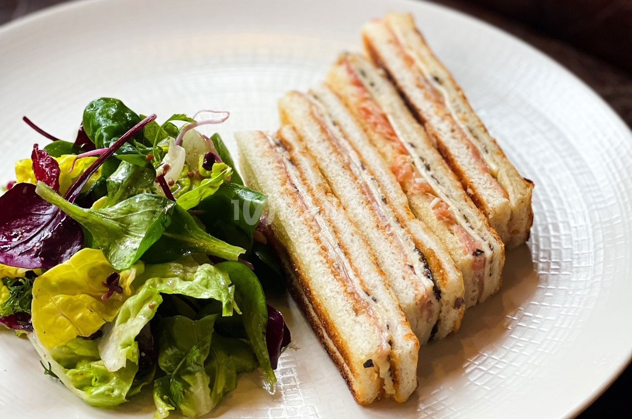 Assiette contenant un sandwich club tranché accompagné d'une salade verte variée.