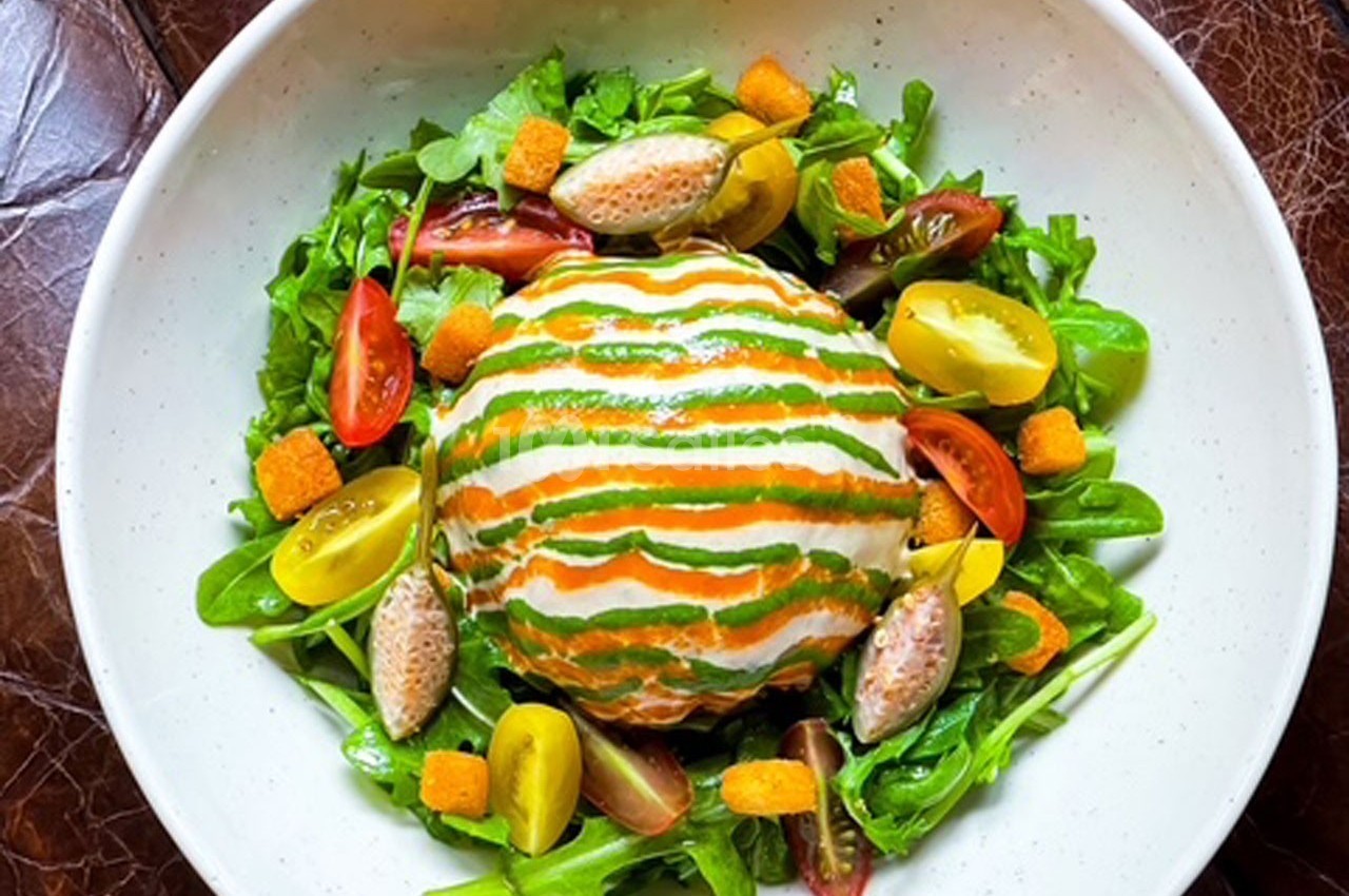 Salade colorée avec légumes frais, croûtons, quenelles et une boule garnie de sauce verte et orange.