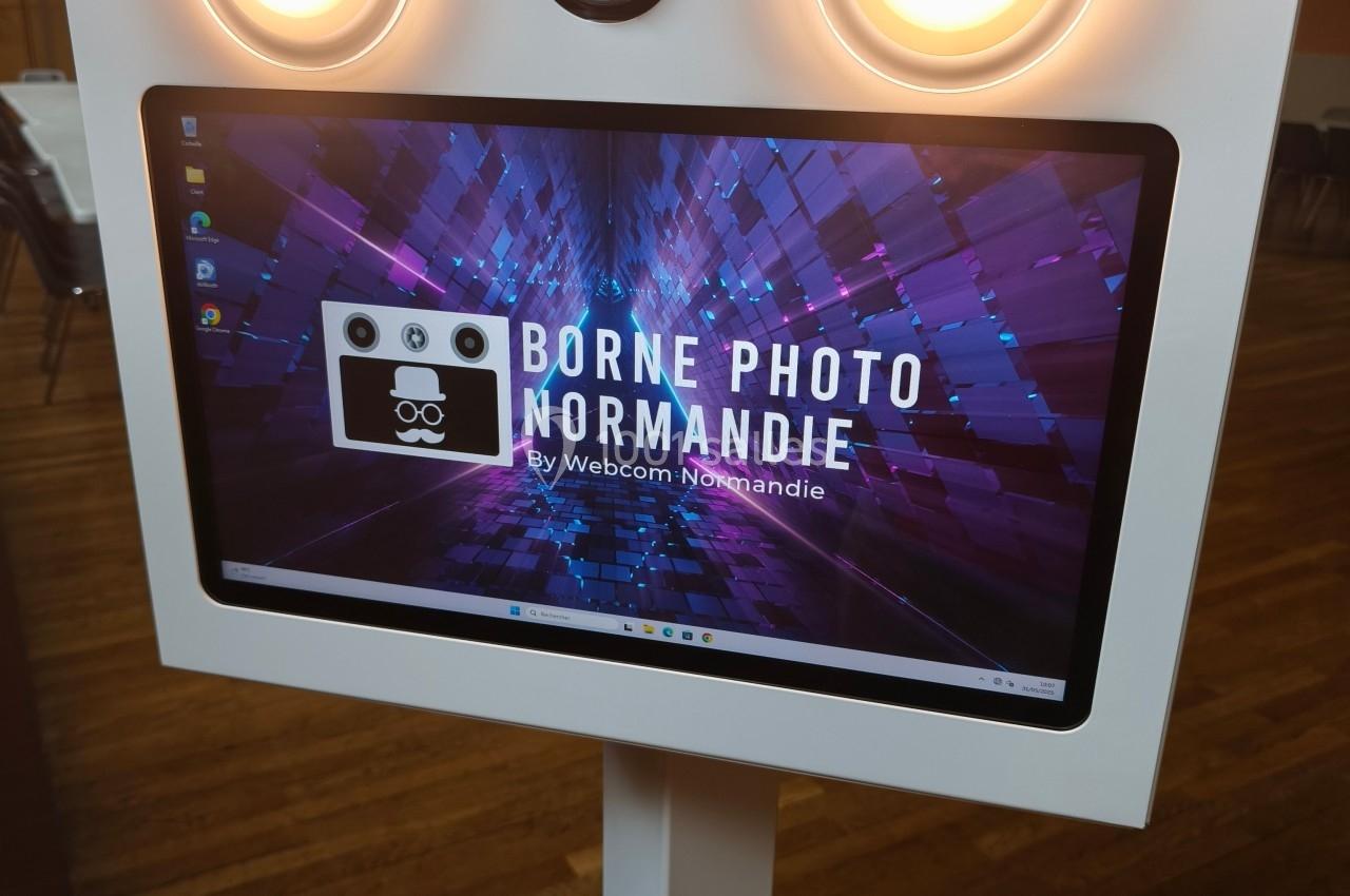 Borne photo interactive blanche avec écran tactile et éclairages circulaires, posée sur un sol en bois.