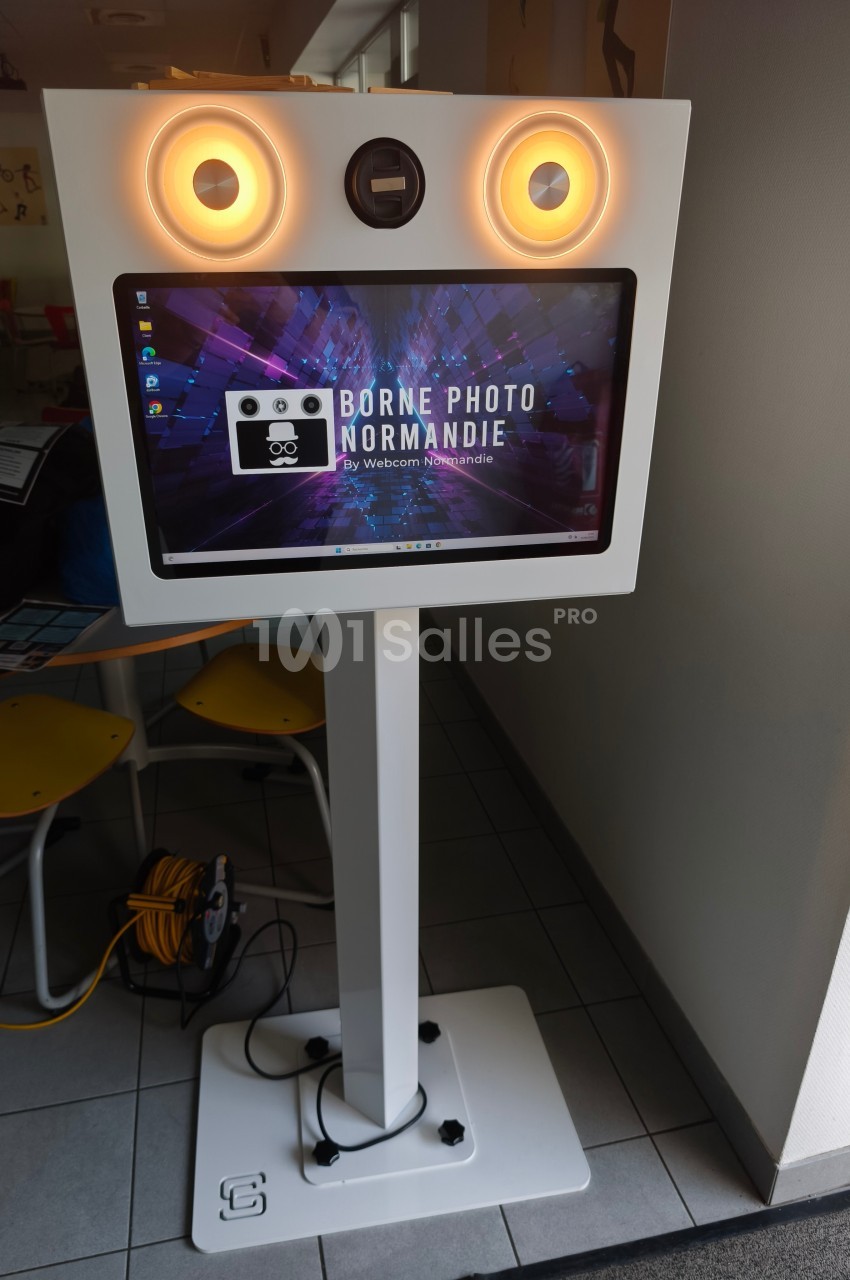 Borne photo interactive sur pied avec écran tactile et éclairage circulaire, installée dans un espace intérieur.