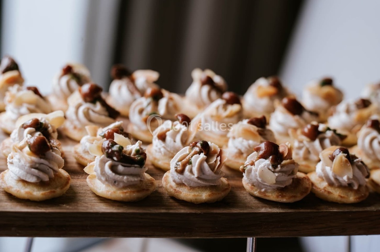 Plateau de mini-bouchées garnies de crème et de noix, présenté sur une planche en bois.