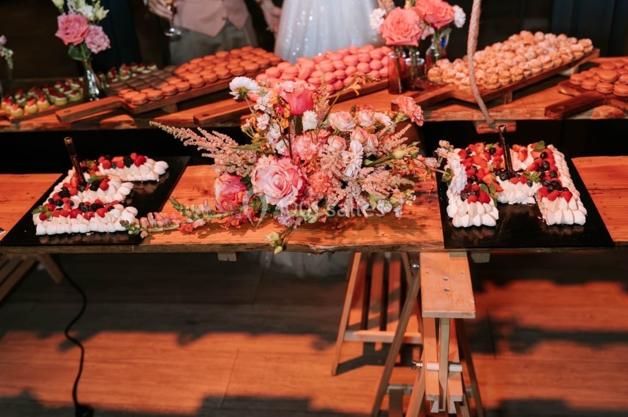 Décoration de table avec des desserts, des fleurs roses et des gâteaux disposés sur des plateaux en bois.