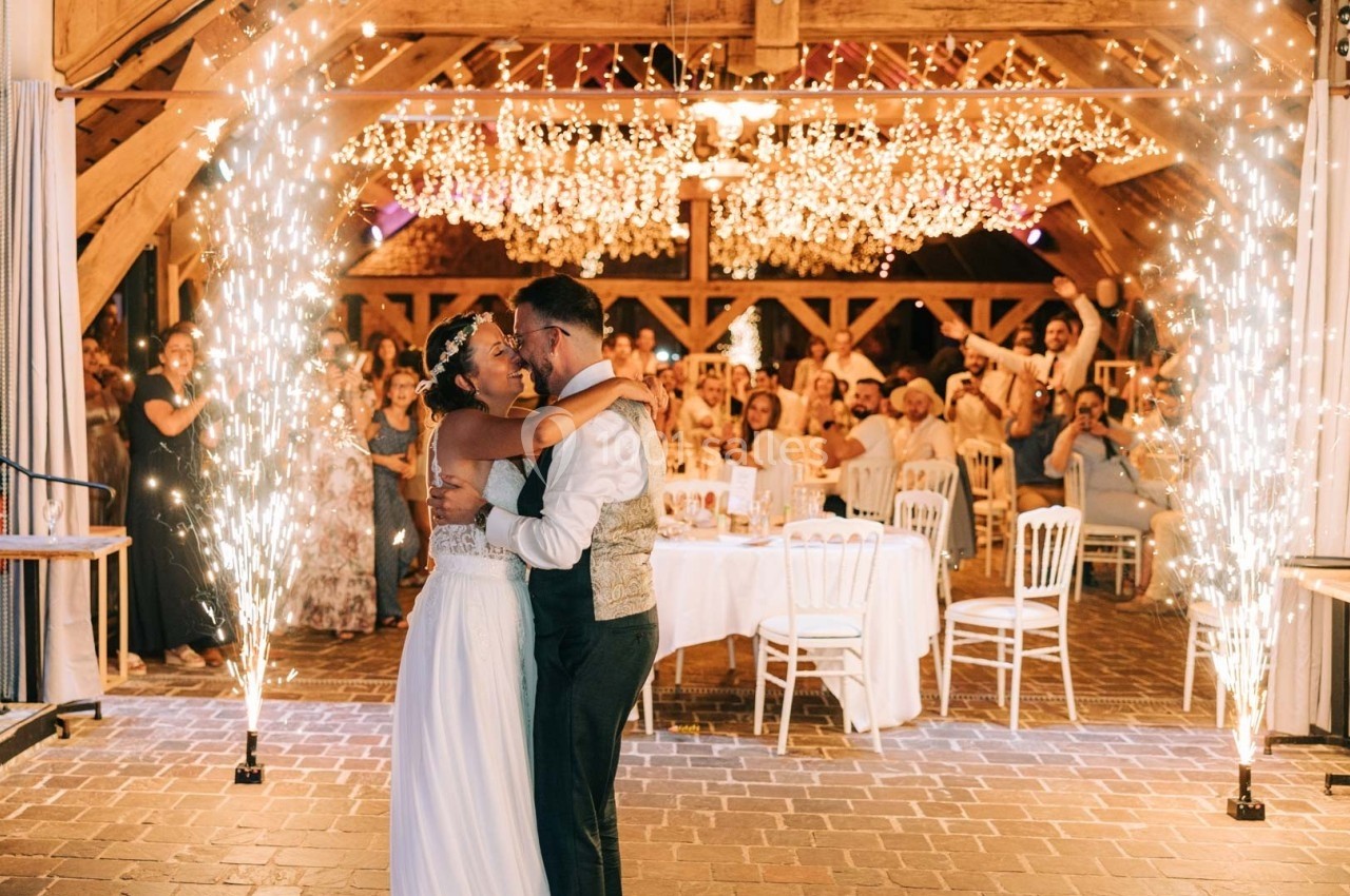 Un couple danse sous des étincelles dans une salle décorée de guirlandes lumineuses, entouré d'invités assis.