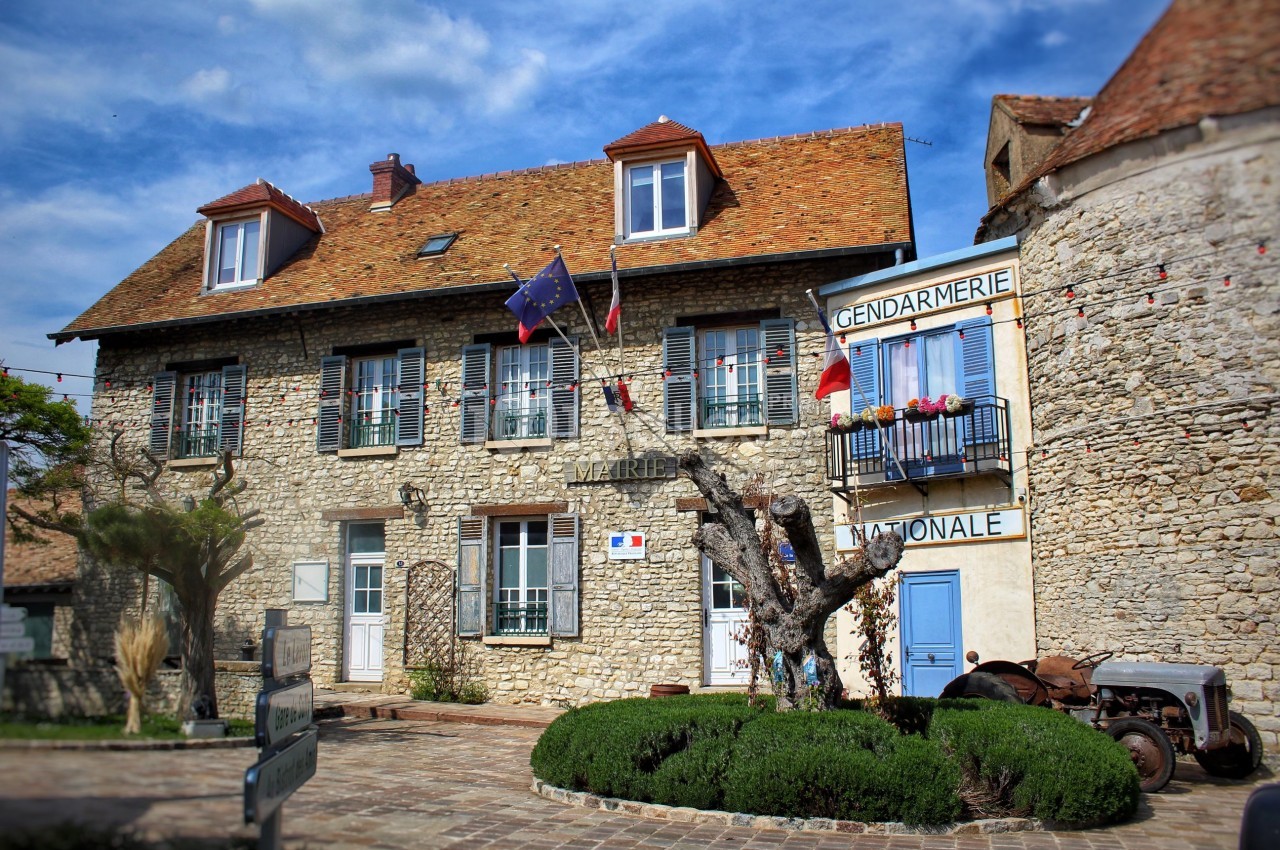 Bâtiment en pierre abritant une mairie et une gendarmerie, décoré de drapeaux français et européen.
