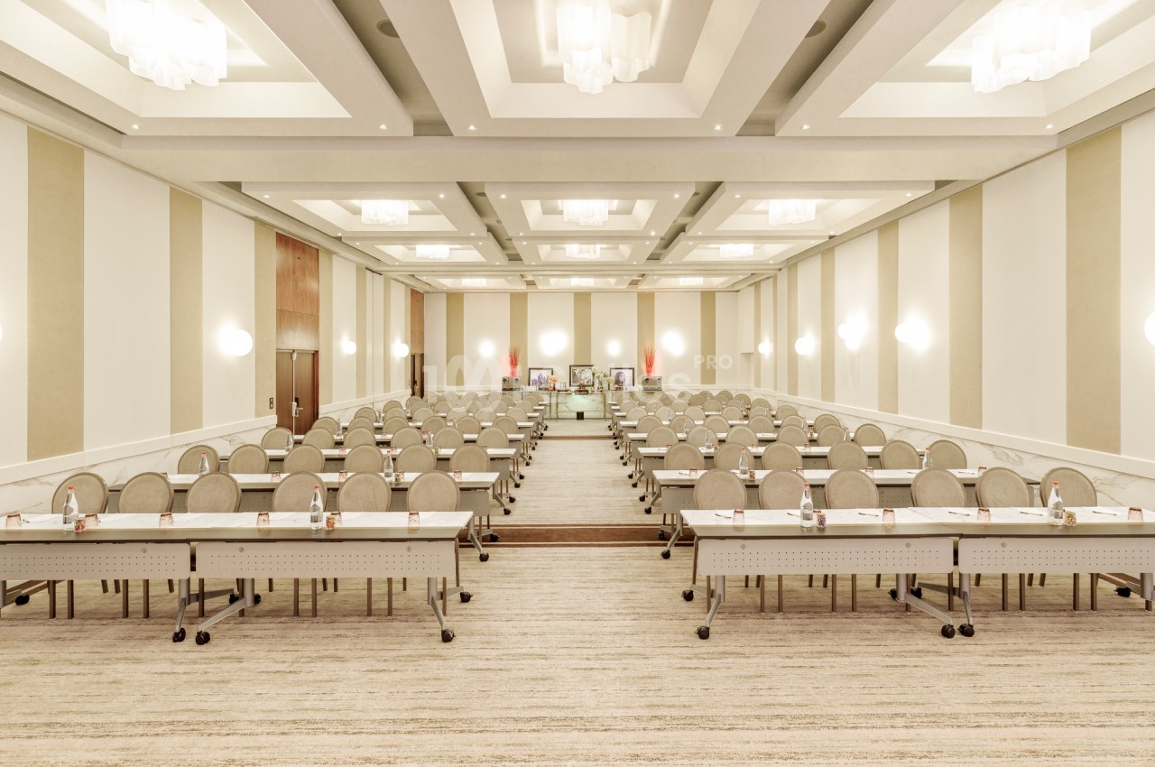 Salle de conférence lumineuse avec rangées de tables et chaises alignées, prête pour une réunion ou un séminaire.