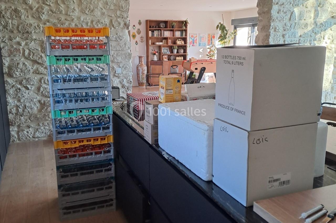 Des caisses de bouteilles et des cartons empilés dans une pièce lumineuse avec des murs en pierre apparente.