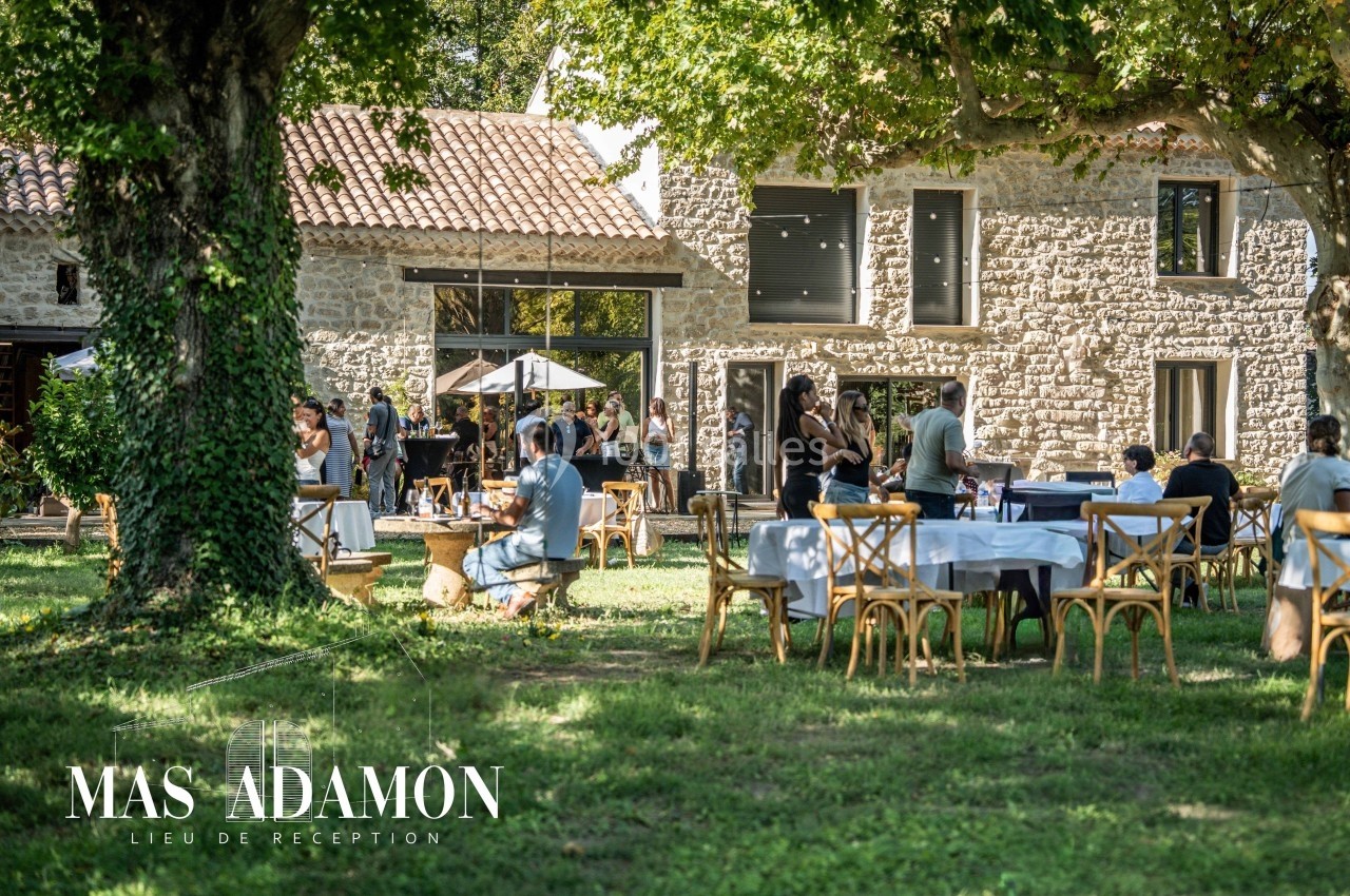 Personnes rassemblées dans un jardin verdoyant avec des tables dressées, devant un bâtiment en pierre.