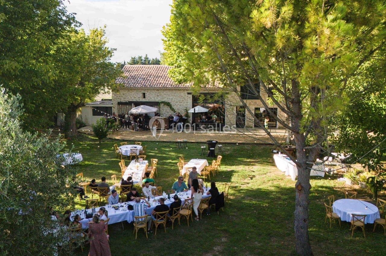 Vue d'un jardin avec des tables dressées et des invités lors d'un événement près d'une maison en pierre.