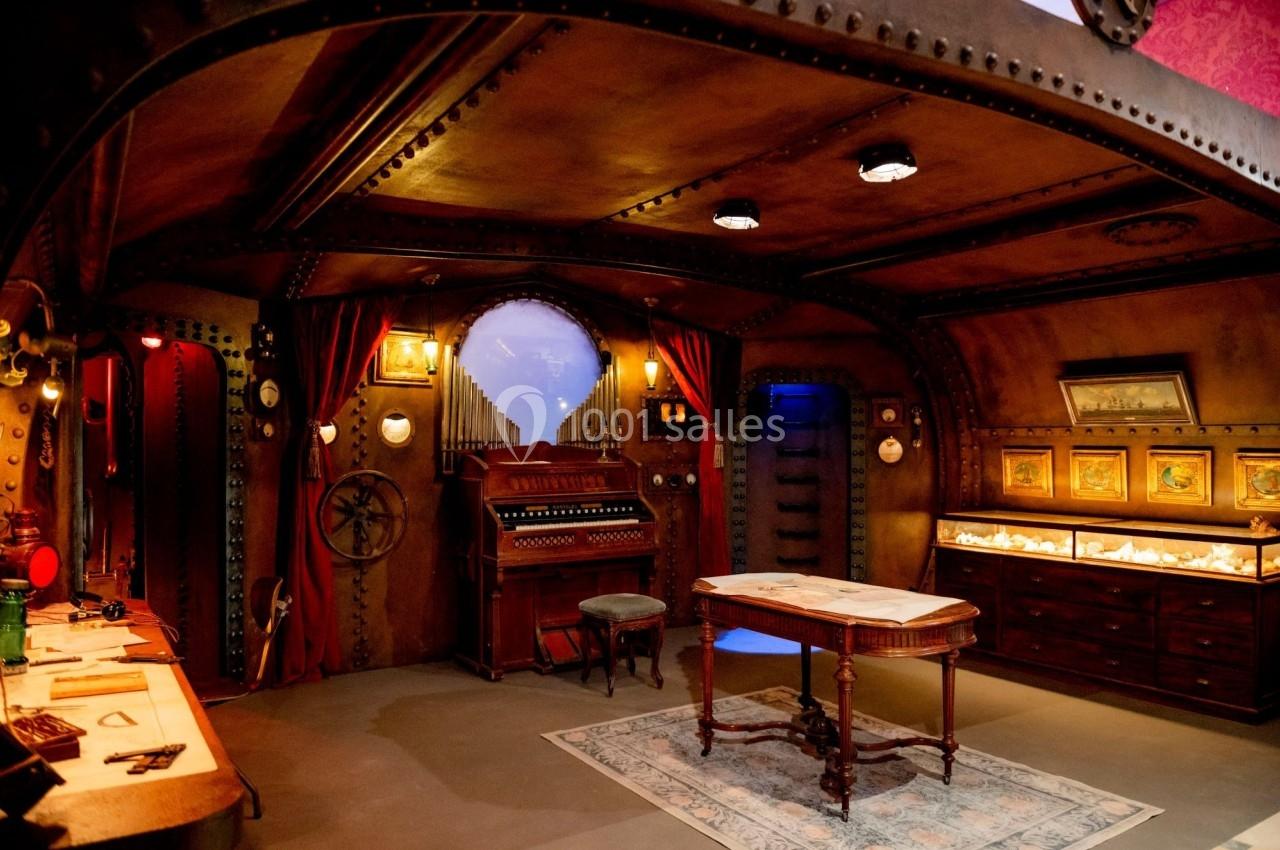 Salle au style steampunk avec orgue, table centrale, vitrines éclairées et décorations en métal et bois.