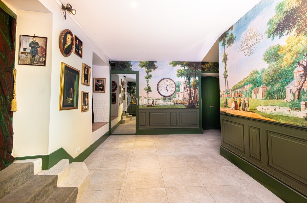 Intérieur lumineux avec murs décorés de peintures murales et cadres, sol en carrelage clair et horloge murale centrale.