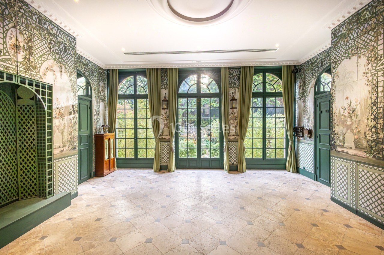 Salle lumineuse avec grandes fenêtres cintrées, murs ornés de motifs végétaux et sol en pierre claire.