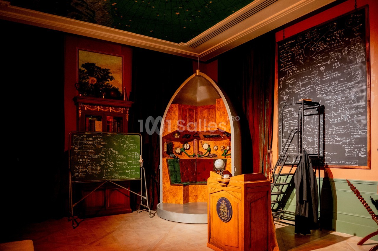Salle avec décor scientifique, tableau noir rempli d'équations, maquette en bois et pupitre en avant-plan.