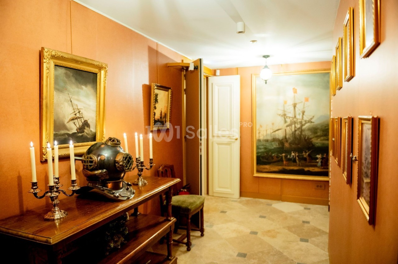 Salle décorée avec des tableaux maritimes, un casque de scaphandrier ancien et des chandeliers sur une table en bois.