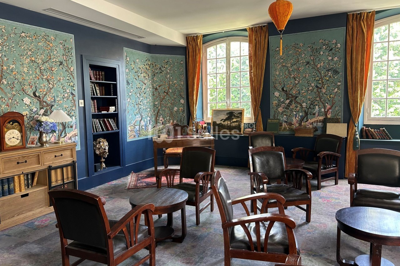 Salle de lecture lumineuse avec fauteuils en bois, tables basses, bibliothèque et murs décorés de motifs floraux.
