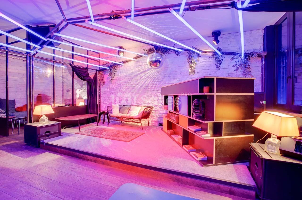 Espace intérieur moderne avec éclairage néon coloré, canapé, étagères et décorations murales végétales.
