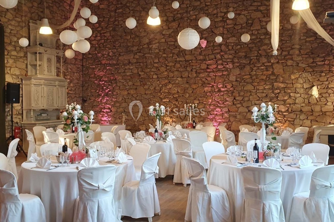 Salle de réception décorée avec des tables rondes, nappes blanches, chandeliers et lanternes suspendues.