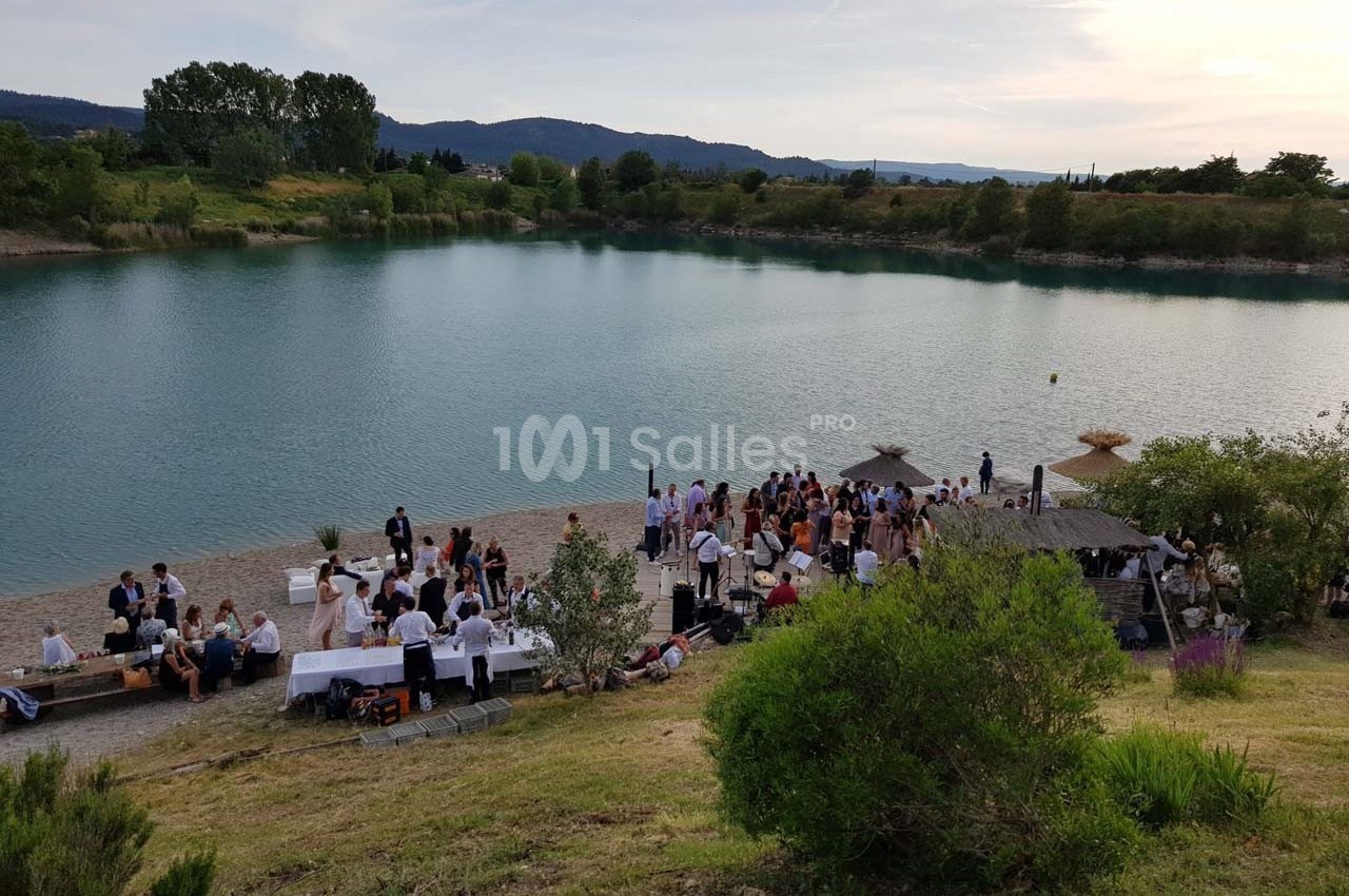 Groupe de personnes réunies sur une plage au bord d'un lac, avec des tables dressées et un paysage naturel en arrière-plan.