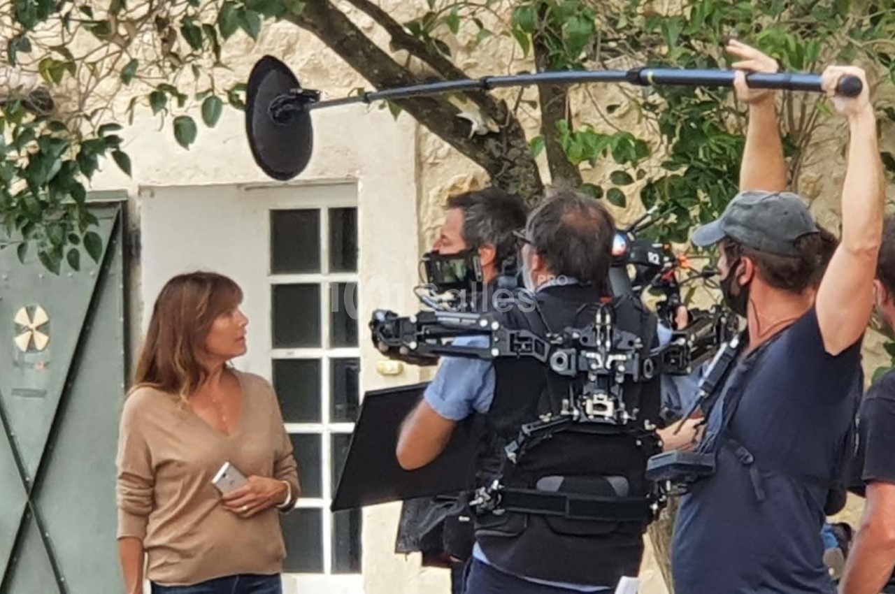 Une femme échange avec une équipe de tournage équipée d'une caméra et d'une perche micro en extérieur.