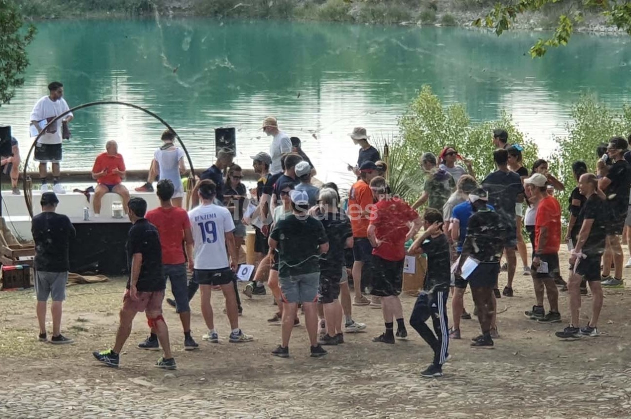 Groupe de personnes rassemblées en plein air près d'un lac, avec une scène et des intervenants en arrière-plan.