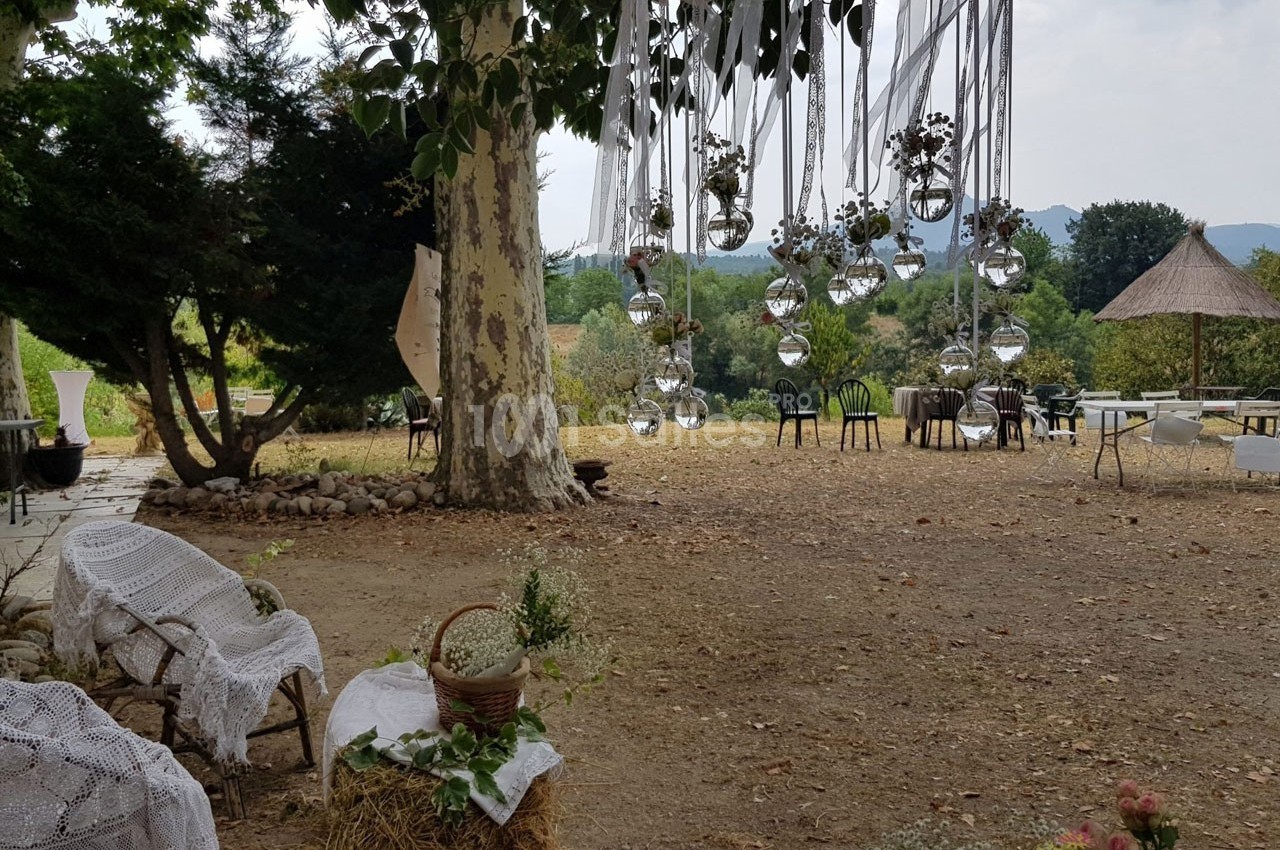 Décoration extérieure avec suspensions en verre sous un arbre, chaises et tables disposées sur un terrain naturel.