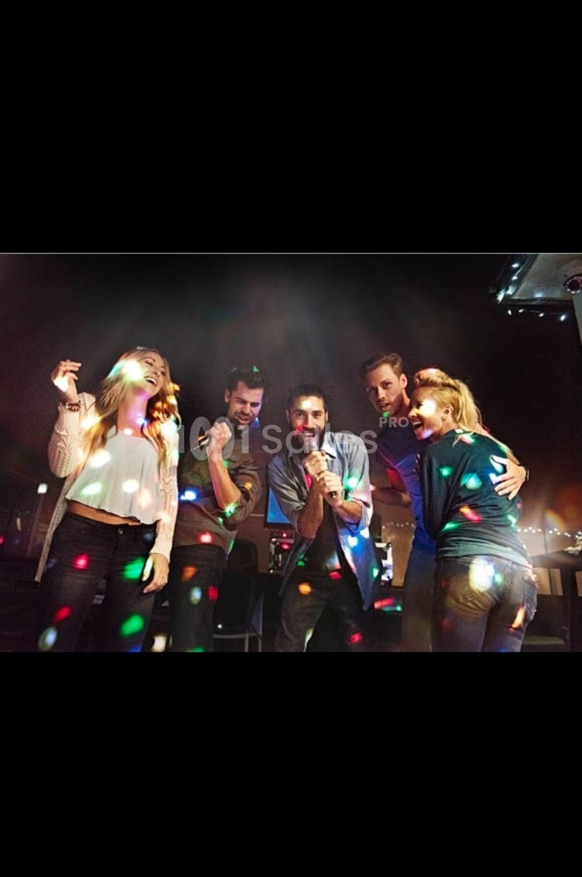 Des personnes chantent et dansent sous des lumières colorées dans une ambiance festive en intérieur.