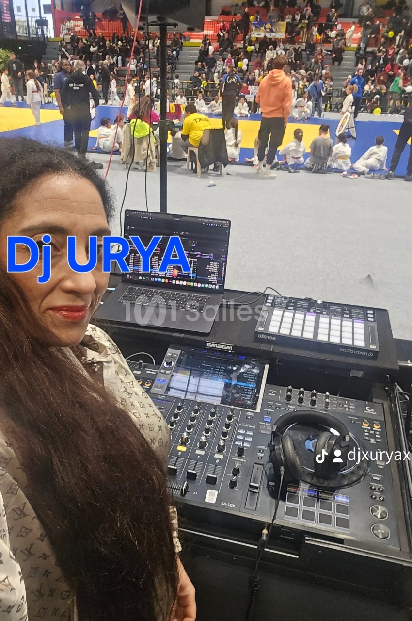 Femme devant une table de mixage avec ordinateurs, dans une salle où se déroule un événement sportif ou culturel.