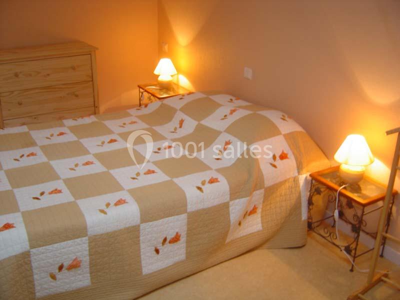 Lit double avec couvre-lit à motifs de feuilles orange, entouré de deux tables de chevet avec lampes allumées.