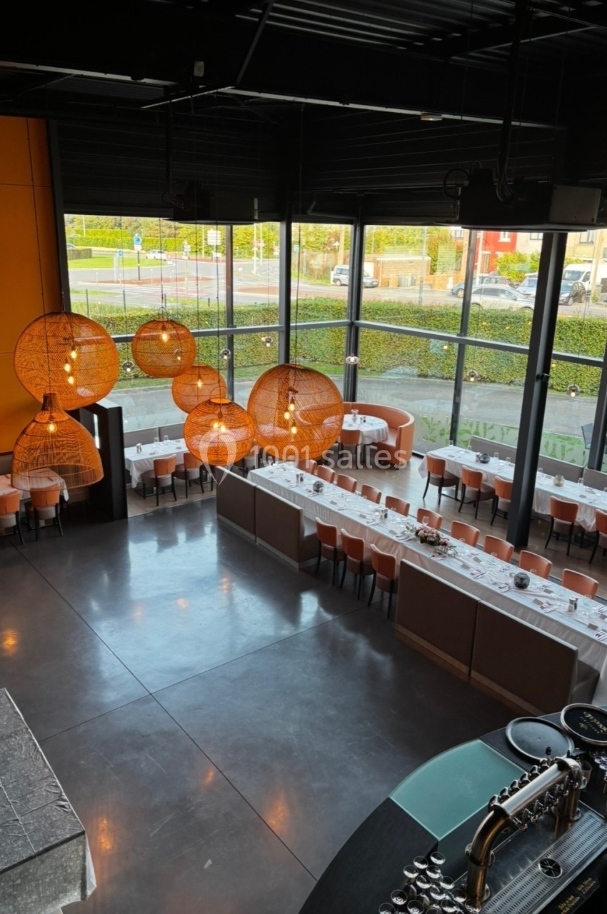 Salle de restaurant moderne avec grandes baies vitrées, tables dressées et luminaires suspendus en rotin.