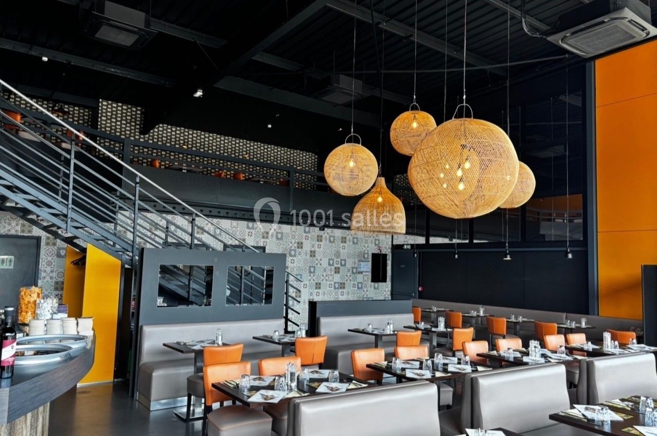Salle de restaurant moderne avec mobilier en cuir, luminaires suspendus en osier et escalier métallique.