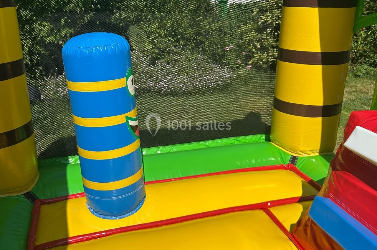 Structure gonflable colorée avec un obstacle cylindrique bleu et jaune, située dans un jardin verdoyant.