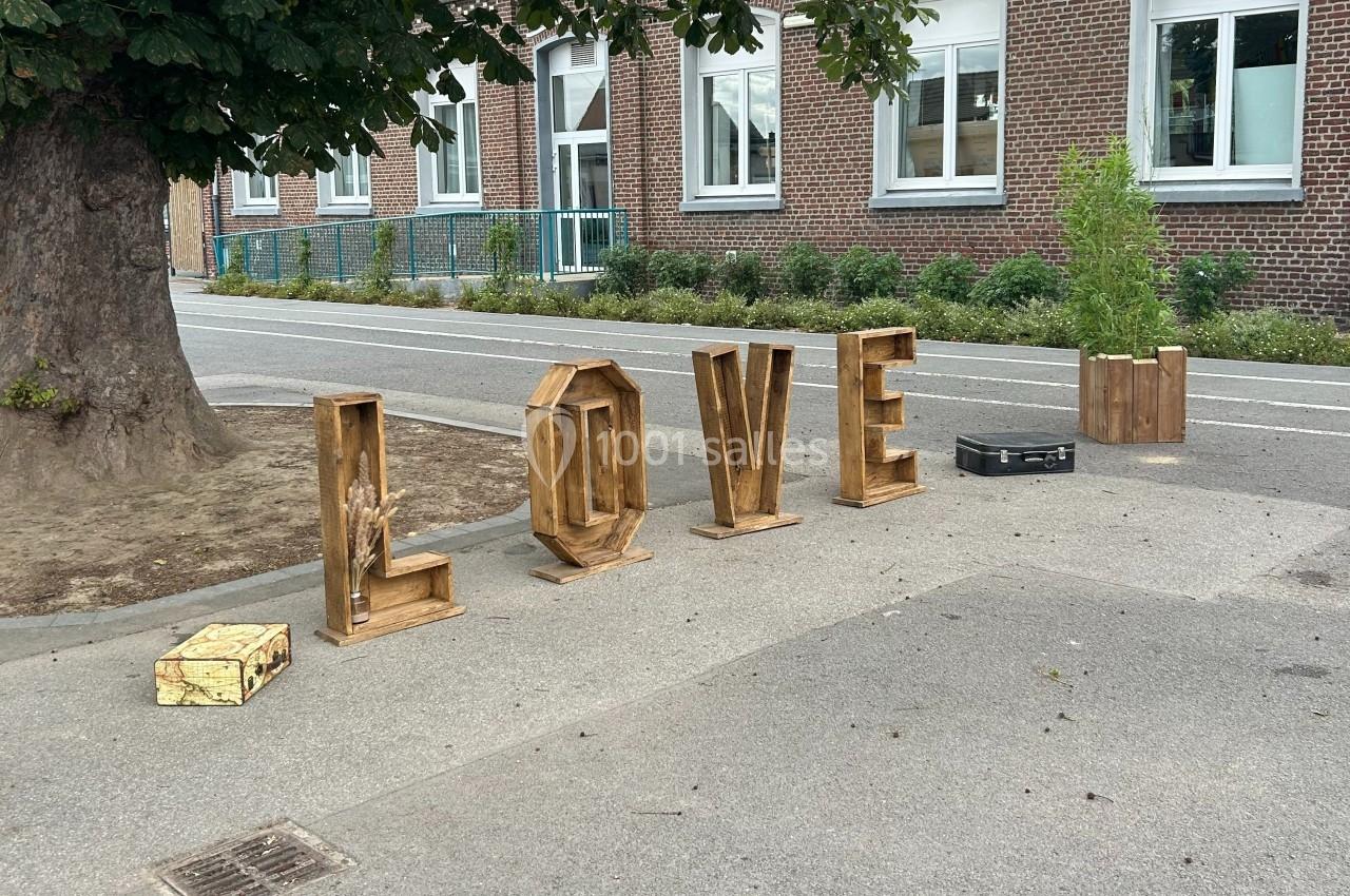 Lettres en bois formant le mot ’LOVE’ disposées sur un trottoir devant un bâtiment en briques.