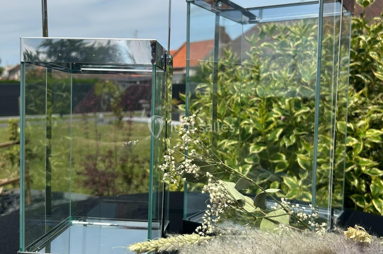 Deux lanternes en verre transparent posées sur une table noire, entourées de végétation et de fleurs séchées.
