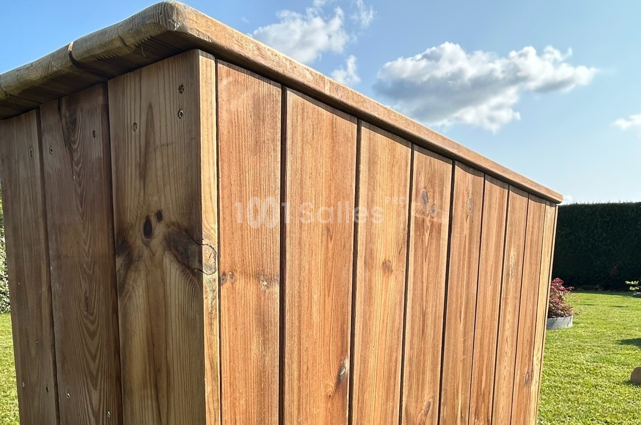 Vue rapprochée d'un abri en bois dans un jardin, avec ciel bleu et quelques nuages en arrière-plan.