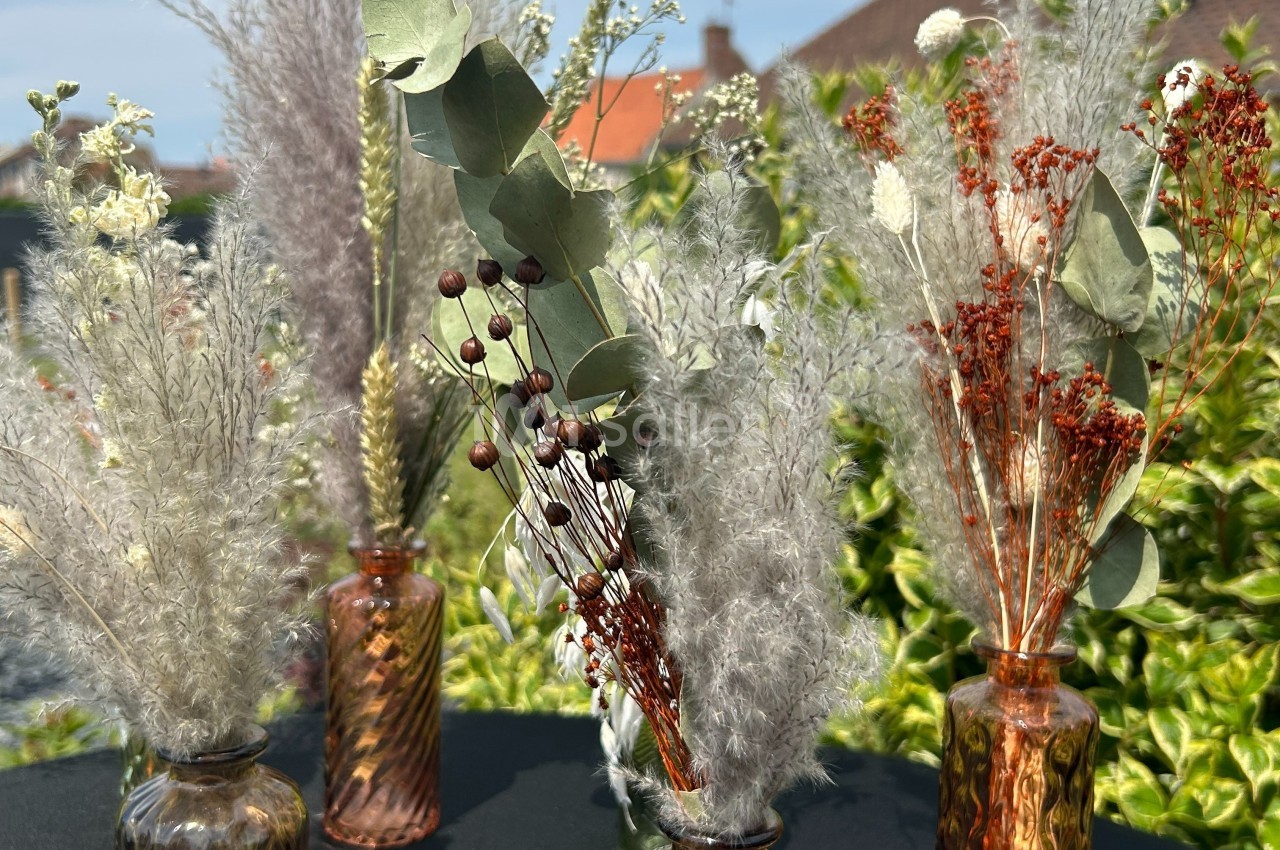 Bouquets de fleurs séchées variées disposés dans des vases en verre marron, avec un fond de jardin verdoyant.