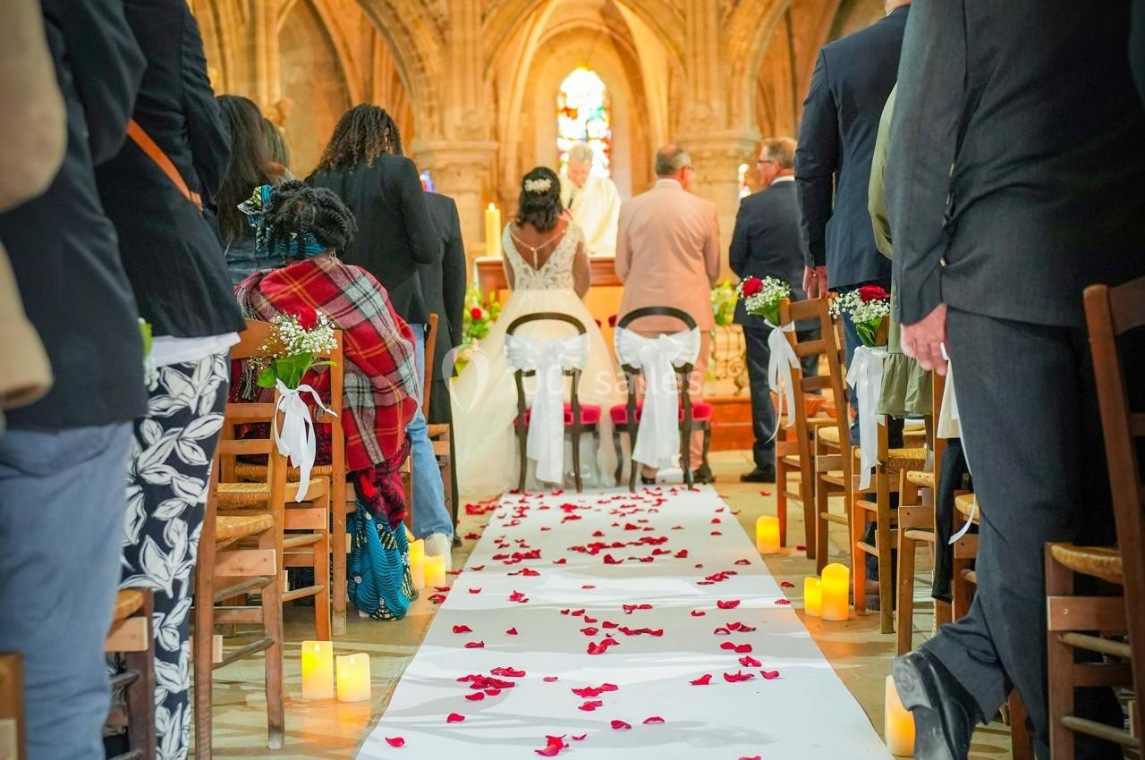 Cérémonie de mariage dans une église, avec des invités assis et une allée décorée de pétales de rose rouges.