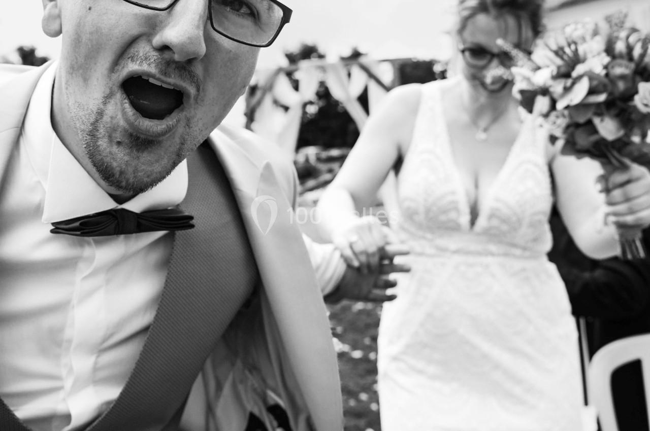 Un homme en costume s'exclame face à l'objectif tandis qu'une femme en robe de mariée tient un bouquet.