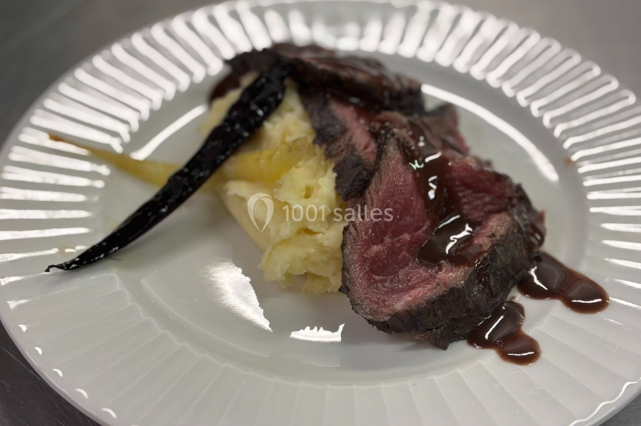 Assiette contenant une tranche de viande saignante, purée de pommes de terre et carottes glacées, nappée de sauce.