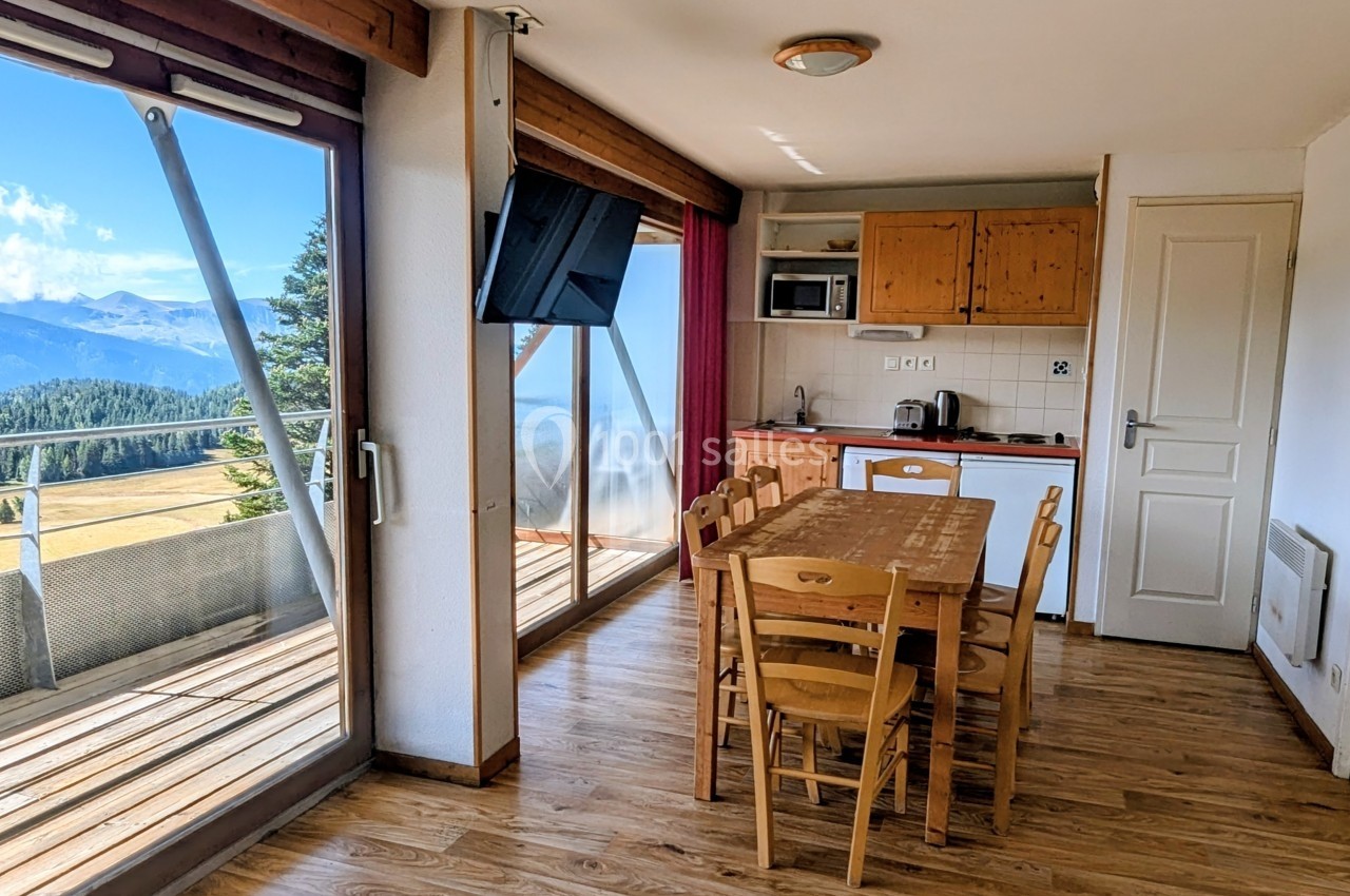 Salle à manger avec table en bois, cuisine équipée et grande baie vitrée offrant une vue sur les montagnes.