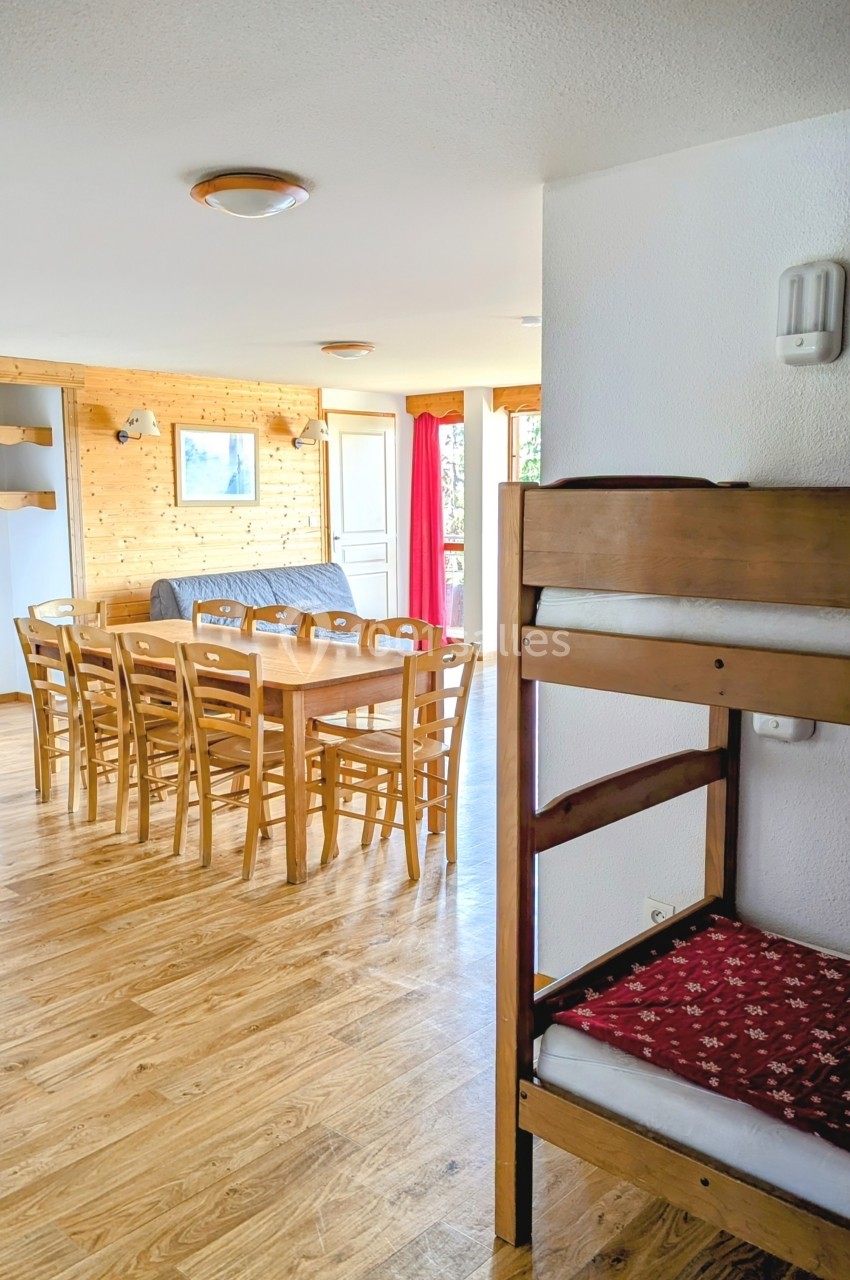 Salle à manger lumineuse avec table en bois, chaises assorties, canapé gris et lits superposés au premier plan.